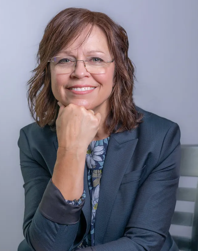 Portrait of Jody Powers smiling, wearing glasses and a navy blazer